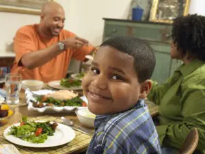 Family Sits at a Table With Food, Boy Looking at Camera